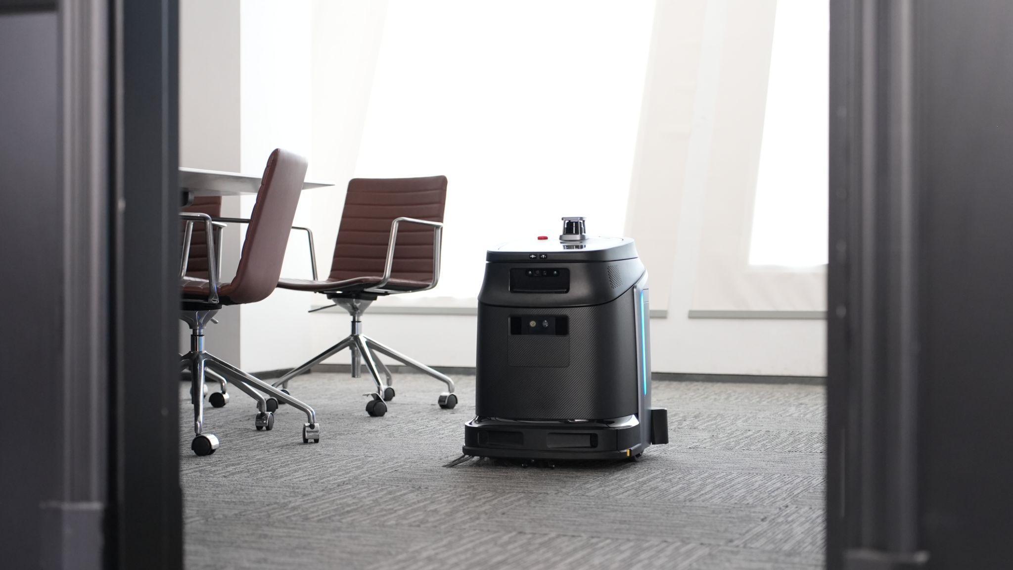 Gausium Phantas cleaning a carpeted office meeting room beside desks and chairs